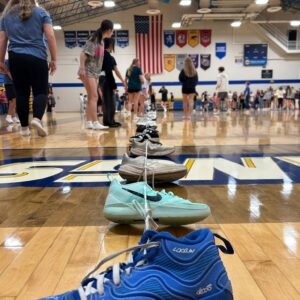 Low-angle shot of a gymnasium with teal sneakers in the foreground and people lined up on the polished floor.